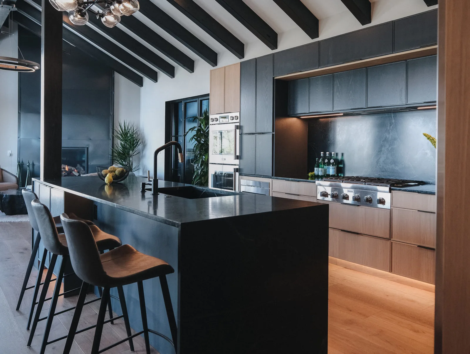 Kitchen with a dark island, timber beams and walnut cabinetry lit from above