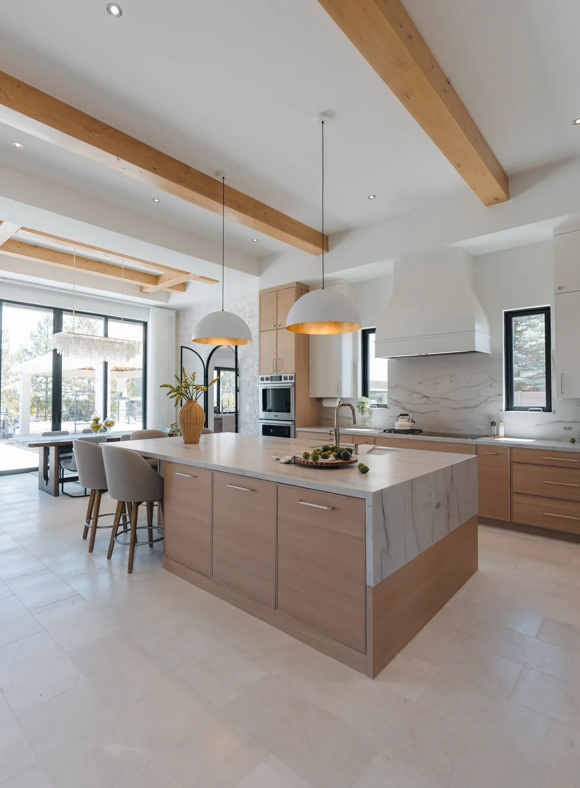 Open kitchen with white oak cabinetry, a stone waterfall island and exposed timber beams