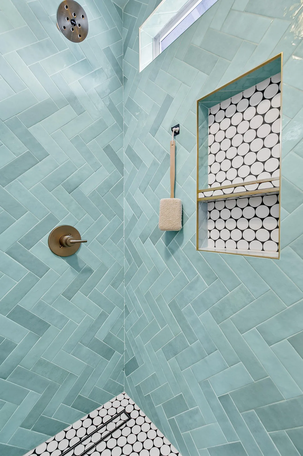 Green herringbone shower tile meeting a hexagonal mosaic niche