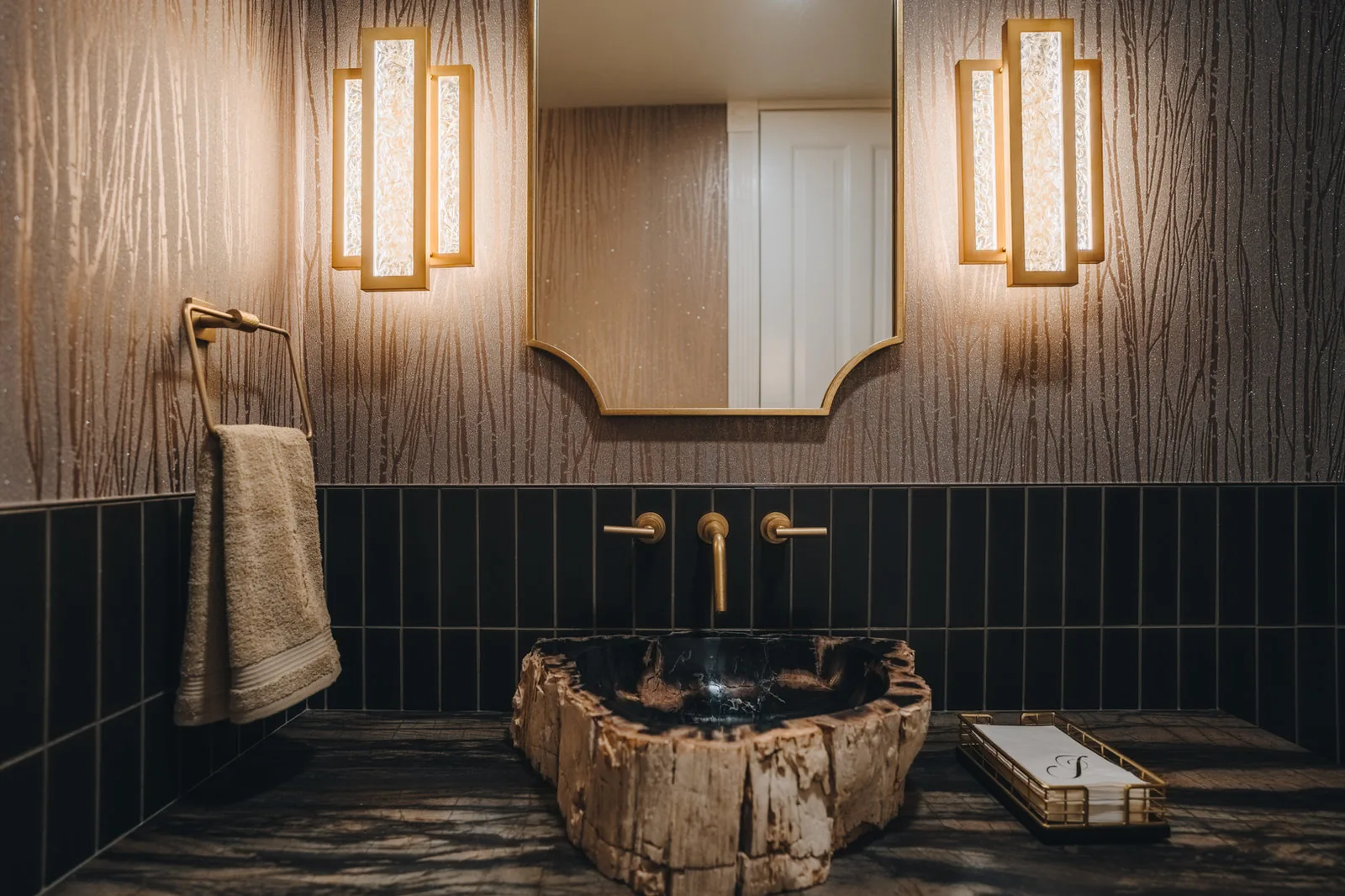 Powder room with a petrified wood vessel sink, brass fittings and stacked dark tile