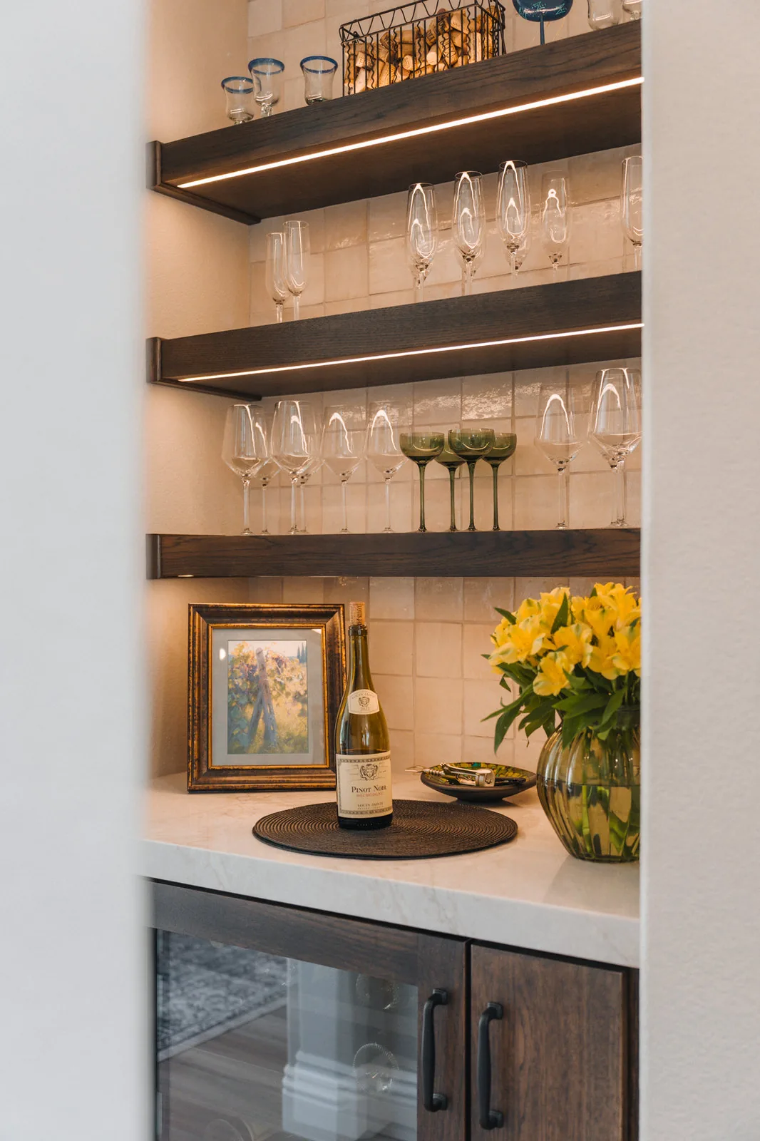 Built-in wine bar with walnut shelving, lit glassware and stone counter
