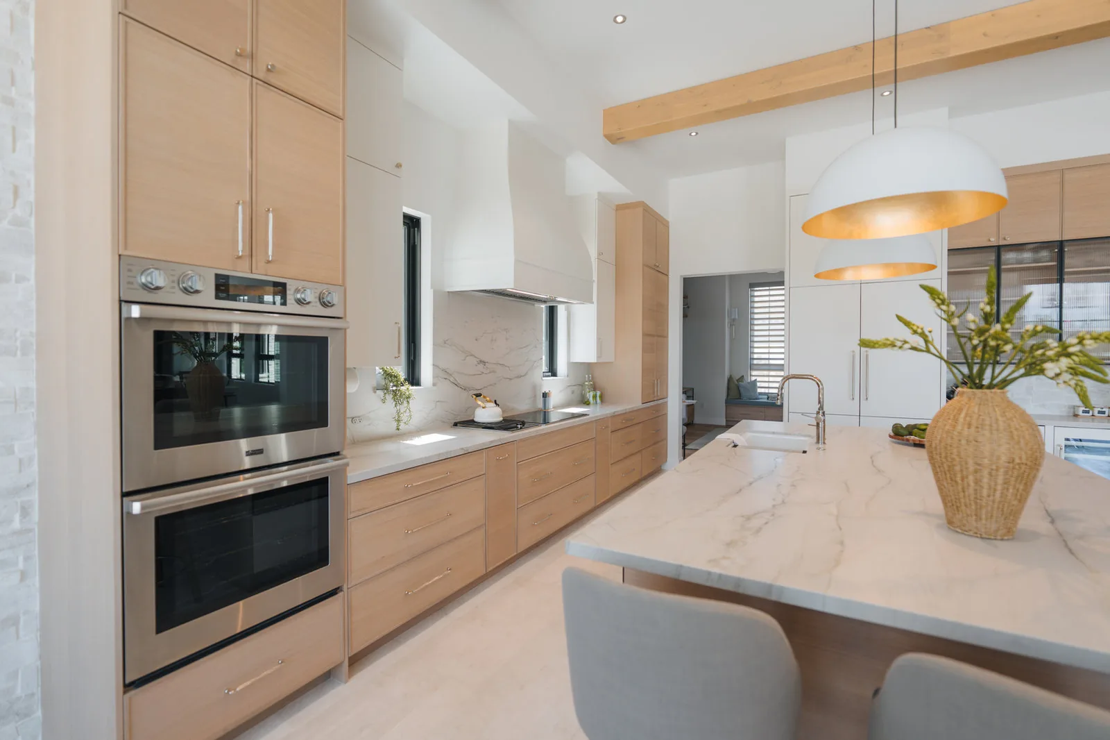 White oak kitchen with a marble island, brass-lined pendants and integrated appliances
