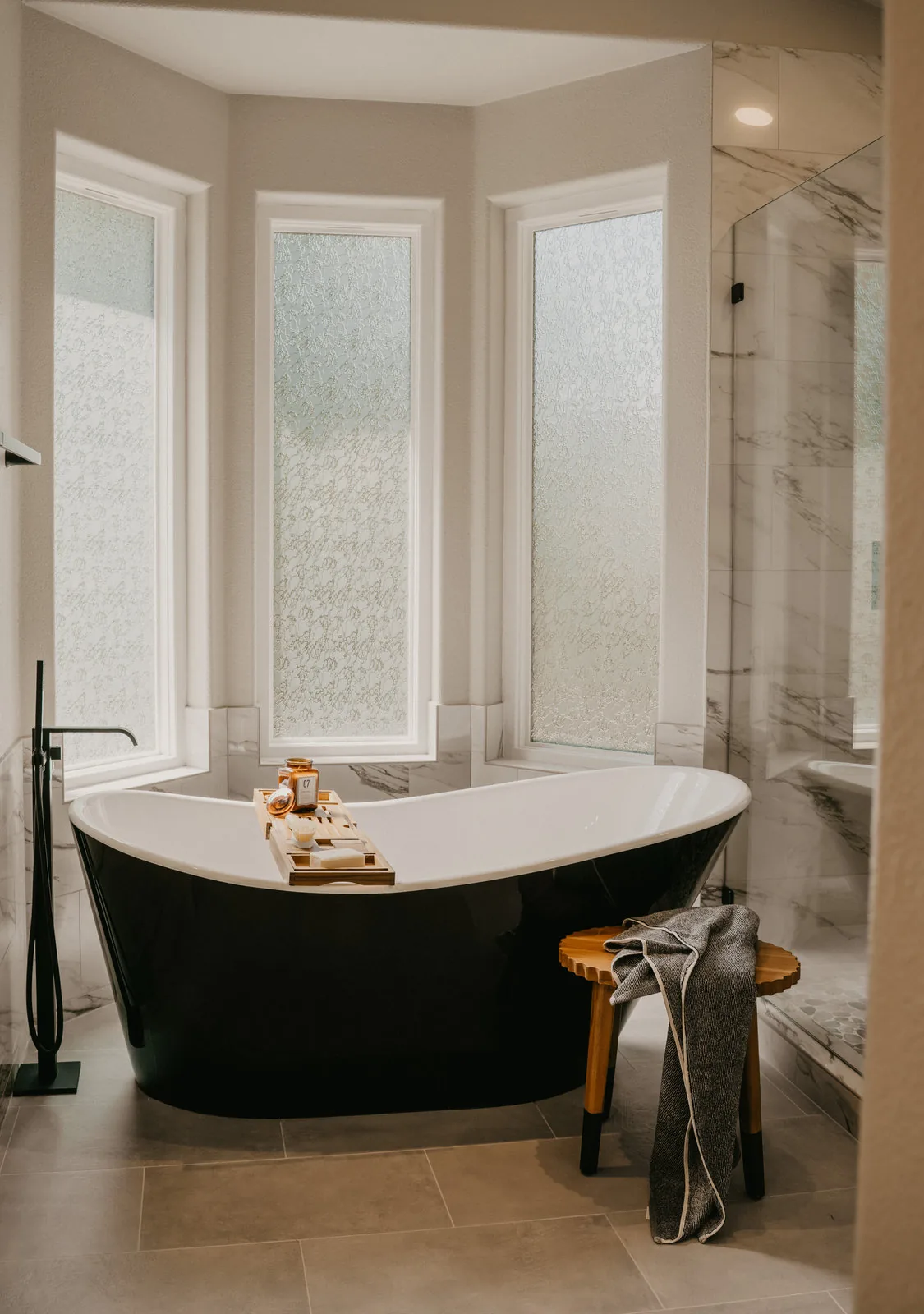 Freestanding black soaking tub in a marble bathroom