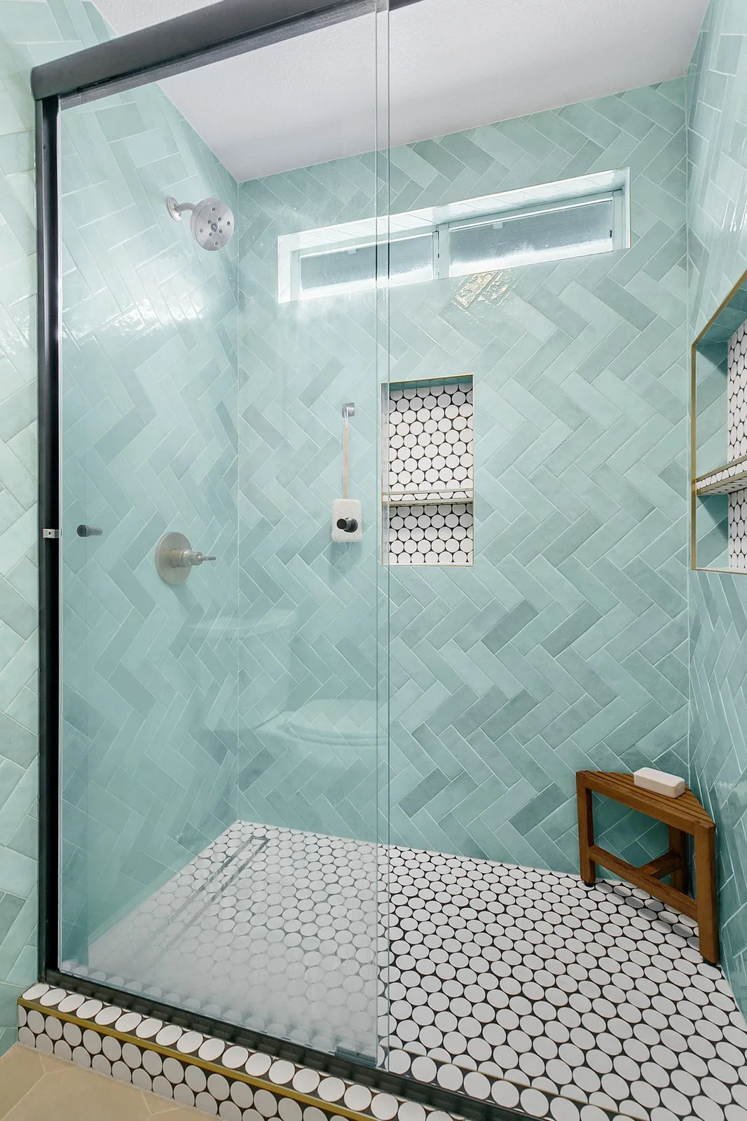 Walk-in shower with sea green herringbone tile and a mosaic floor
