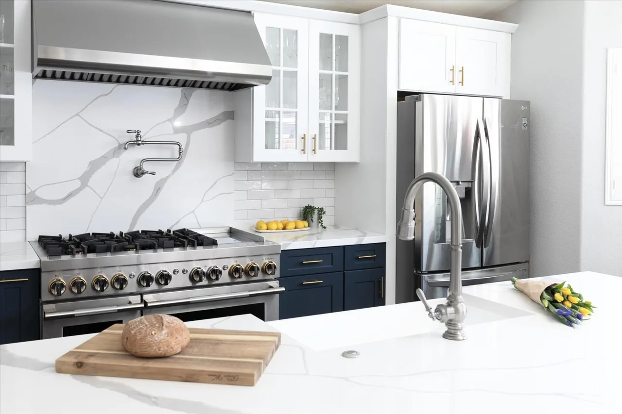 Kitchen with navy lower cabinets, marble backsplash and a pot filler