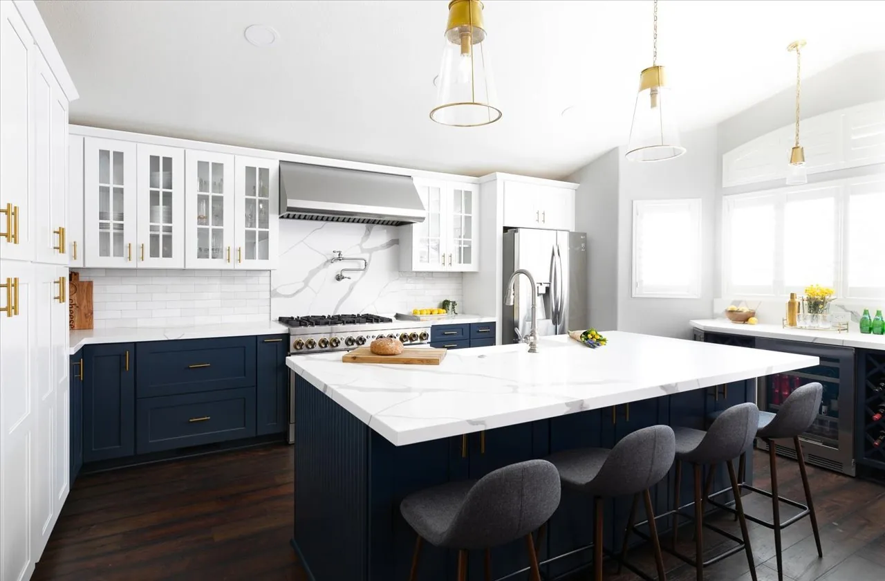 Navy island kitchen with white perimeter cabinets and brass pendants