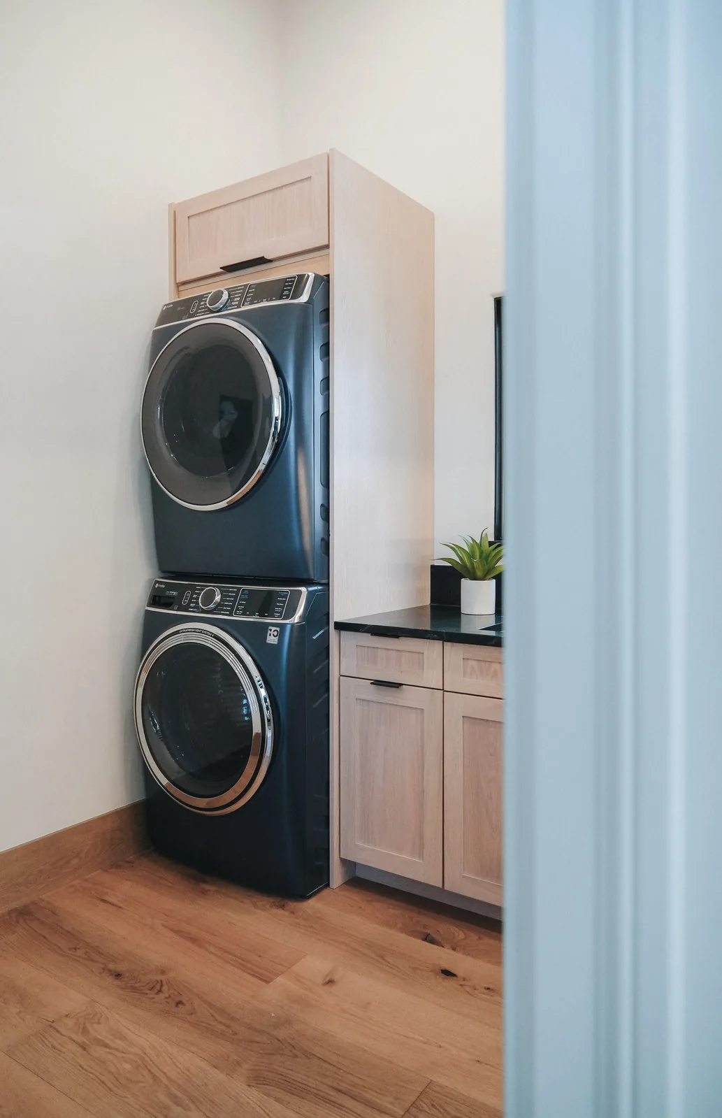 Laundry room with stacked machines and light oak cabinetry